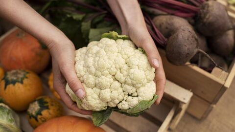 Person nimmt Blumenkohl mit beiden Händen aus einer Gemüsekiste
