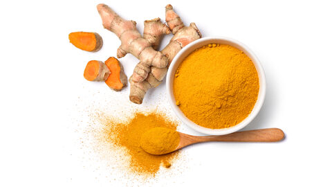 Kurkumagewürz in Schale und auf einem Holzlöffel von oben, dadrüber Kurkumaknolle