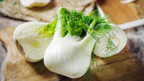 Ein ganzer und ein aufgeschnittener Fenchel auf einer Holzplatte