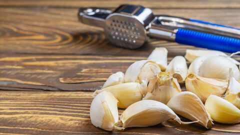 Knoblauchpresse und Knoblauchzehen auf einem Holzbrett 