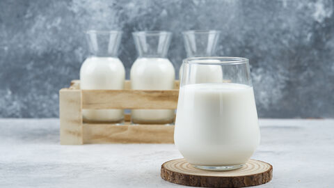 Ein Glas mit Milch im Vordergrund, drei Karaffen mit Milch im Hintergrund