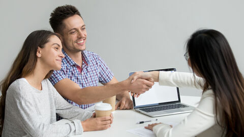 Ein junges Paar sitzt in der Beratung und der Mann reicht der Beratungskraft die Hand