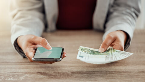 Mann hällt ein Smartphone und Geldscheine in seinen Händen
