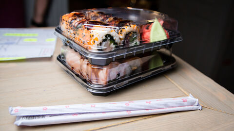 Sushi in Plastikbox und in Papier verpachte Essstäbchen