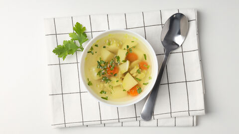 Eine Schüssel mit Eintopf steht auf einem gefalteten Küchenhandtuch, daneben liegt ein Löffel