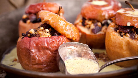 Bratäpfel un Vanillesoße in einer Backform. Im Vordergrund liegt eine Schöpfkelle.