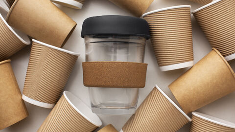 Ein Mehrwegbecher liegt zwischen vielen Einwegbechern
