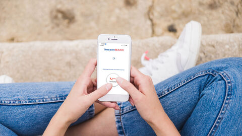 Frau hält Smartphone mit HessenWarn App 
