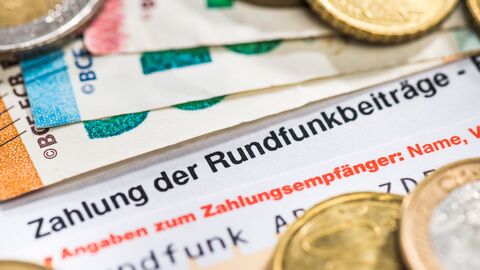 Münzen und Geldscheine liegen auf Überweisungsträger zur Zahlung der Rundfunkgebühr