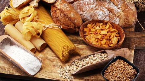 Verschiedene Vollkornprodukte: Brot, Toas, Nudeln, Mehl, Hafefflocken, Cornflakes, Korn auf einer Holzplatte angerichtet