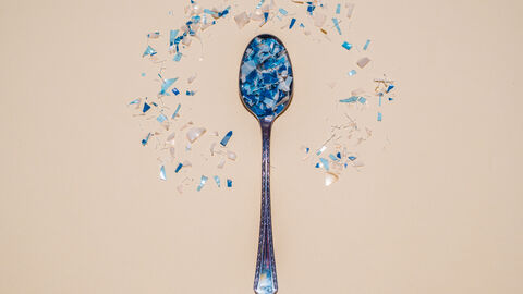 Silberlöffel mit blauen Mikroplastikteilen drauf. Um den Löffel liegen noch weitere blaue Mikroplastikteile verstreut.