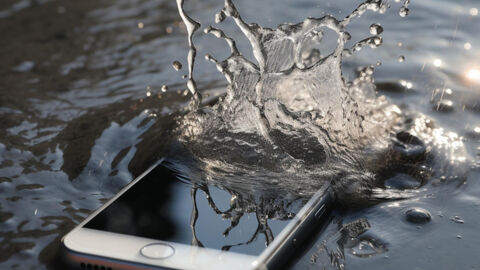 Ein Handy fällt ins Wasser. Tropfen soritzen hoch.