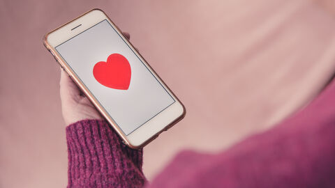 Person hält ein Smartphon ein der Hand. Auf dem Bildschirm erscheint ein rotes Herz.