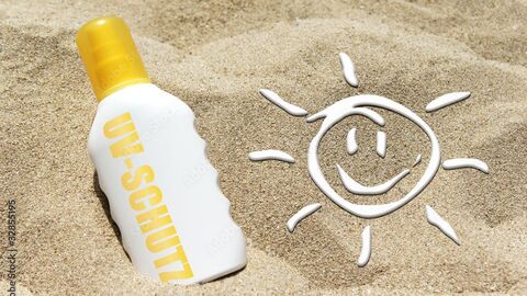 lachendes Smiley aus Sonnencreme und Sonnencremeflasche im Sand
