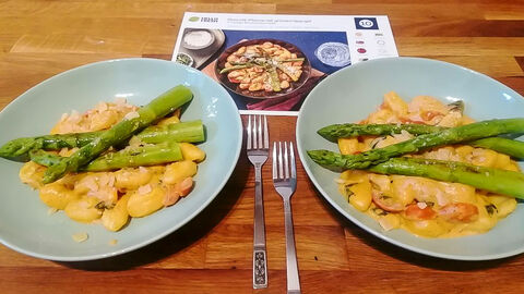 Ergebnis der zubereiteten, gekochten Gnocchi-Pfanne auf Tellern serviert. Daneben Gabeln, hinter den Tellern die passenden Rezeptkarte der Kochbox
