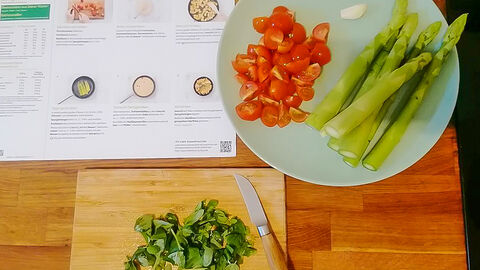 Gnocchi-Pfanne - Erster Schritt der Zubereitung: Tomaten und Basilikum klein schneiden, Spargel und Knoblauchzehe schälen und klein schneiden. Im Hintergrund liegt die Rezeptkarte.
