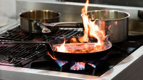 Aus einer Pfanne mit Fleisch auf eingeschaltetem Gasherd lodern Flammen