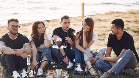 Fünf junge Leute sitzen am Stand, essen Pizza und rauchen Shisha