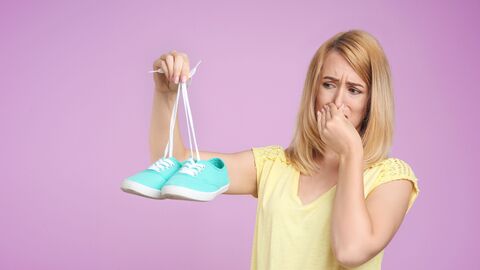 Frau hält sich die Nase wegen unangenehmen Geruch der  Schuhe zu Frau hält ein Paar Schuhe in der rechten Hand, mit der linken Hand hält sie sich die Nase zu