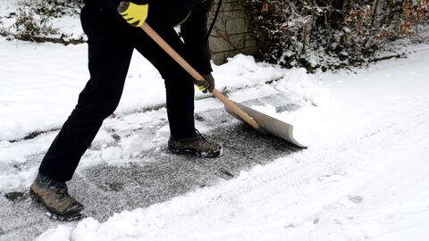 Person räumt mit Schneeschieber Schnee vom Gehweg