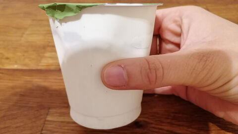Hand mit ungeöffnetem Joghurtbecher 