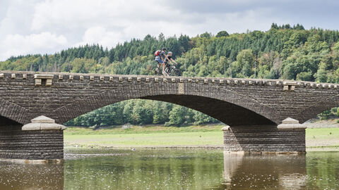 Zwei Radfahrer überqueren eine alte Brücke auf einer Radtour in Nordhessen.