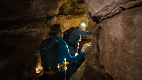Zwei Wanderer durchqueren mit Stirnlampen die dunkle Erdbachhöhle in Breitscheid.