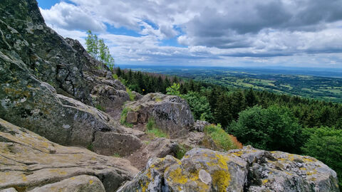 Über eine schroffe Felsformation im Vordergrund weitet sich der Blick auf Wälder und Wiesen im Geotop Bilstein bei Schotten.