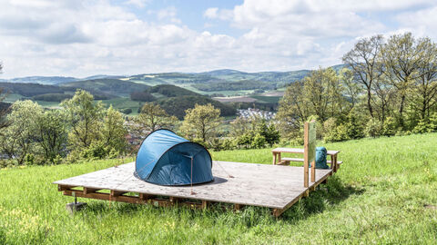 Auf einer grünen Wiese steht eine Holzplattform mit einem Zelt im Trekkingpark Sauerland bei Willingen am Diemelsee