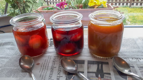 Drei Gläser mit farbiger Sudlösung, in denen sich die zu färbenden Eier befinden