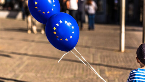 Ein kleiner Junge hält zwei Luftballons mit dem Aufdruck einer Europäischen Flagge