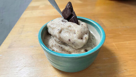 Nice-Cream in einer Porzellan-Schüssel mit einem Stück Schokolade als Garnitur und Löffel.