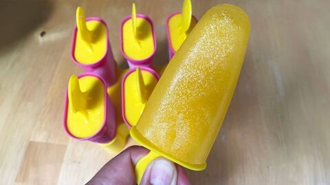 Selbstgemachtes Orangen-Wassereis mit Palstikstiel. Im Hintergrund weitere Eisförmchen für Eis am Stiel.