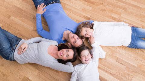 Vater und Mutter liegen mit ihren zwei Kindern im Kreis auf einem Parkettboden