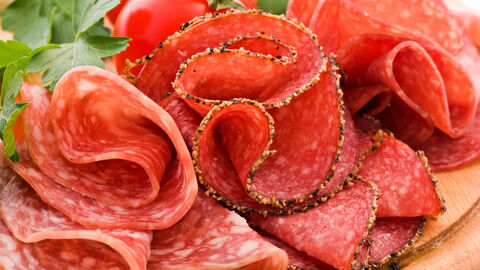 Salami Gerollte Salamischeiben auf einem Holzbrett mit Salatblatt und Tomate im Hintergrund angerichtet
