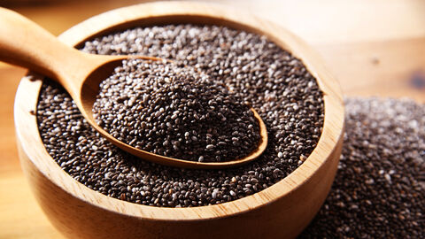Chia-Samen in einer Holzschale. In der Holzschale liegt ein Holzlöffel auf dem ebenfalls Chia-Samen liegen.