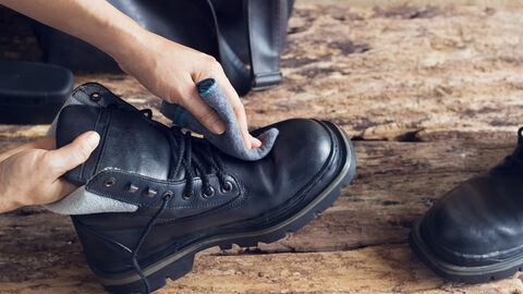 EIne Person putzt schwarze Glattledersteifel mit einem fusselfreien Tuch.