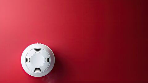 Ein Brandwarnmelder hängt an einer roten Raumdecke