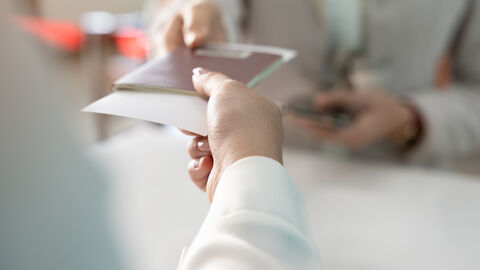 Eine Hand reicht einer anderen Person einen Reisepass mit Flugticket drin