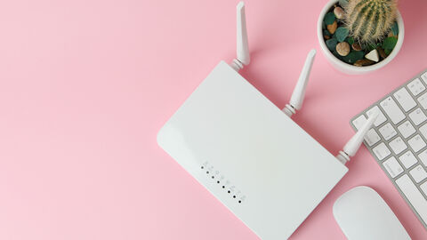 Auf einem Tisch steht ein WLAN-Router. Es ist eine Computermaus und die Ecke einer Tastatur zu sehen. Weiterhin ist ein kleiner Kaktus abgebildet.