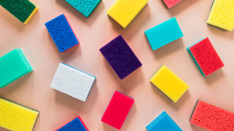 Farblich verschiedene Küchenschwämme liegen unsortiert und in unterschiedlichen Winkeln auf einer glatten Oberfläche
