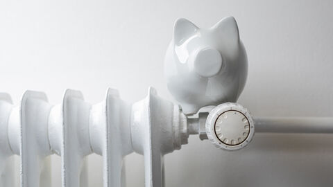 Auf dem Thermostat einer Heizung steht ein weißes Porzellan-Sparschwein.