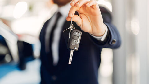 Ein Mann im Anzug (verschwommen dargestellt) hält einen Autoschlüssel in die Kamera