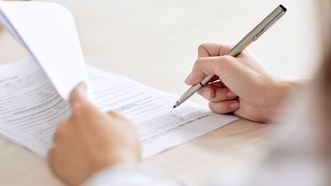 Eine Hand mit Kugelschreiber unterzeichnet einen Vertrag. Die linke hand blättert dazu den Vertrag auf.