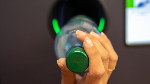 Eine Hand einer Frau steckt eine Pfandflasche in den Rückgabeschacht eines Pfandautomaten