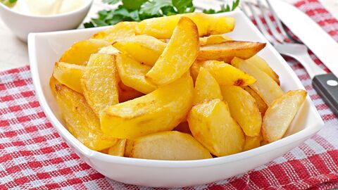 weiße Porzellanschüssel mit gebratenen glänzenden Kartoffelschnitzen steht auf rot-weiß-karierter Tischdecke