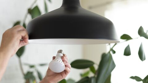 Es sind zwei Hände zu sehen, die eine Lampe in eine Leuchte einbringen. Eine Hand hält die Lampe, die andere die Leuchte