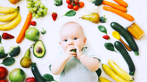 Ein Baby liegt auf dem Rücken zwischen vielen verschiedenen Gemüse und Obstsorten