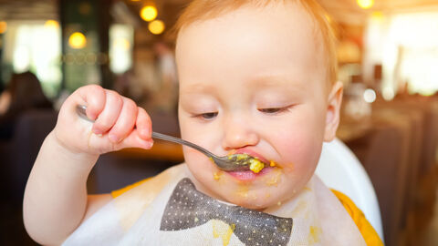 Ein Kind isst selbst mit einem Löffel